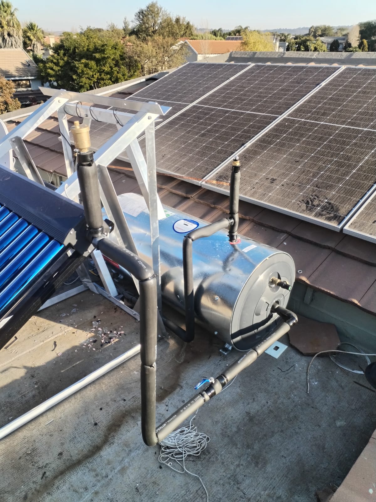 Solar geyser and collector installed on a tiled roof beside solar panels